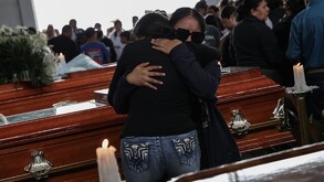 Mujeres vestidas de negro abrazándose frente a un féretro, durante un funeral.