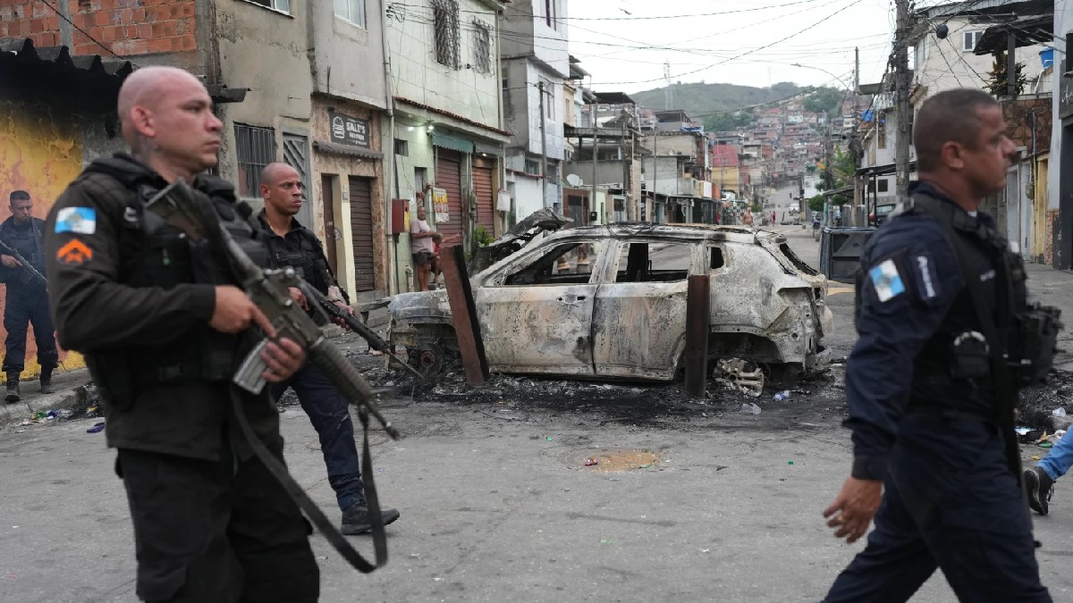Policías con armas pasan frente a un coche quemado que fue utilizado como barricada durante la operación policial en la favela de Brasil