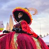 Una mujer vestida de Catrina con un enorme y colorido vestido rojo y un sombrero grande con flores y plumas. Posa al aire libre en el centro de la ciudad Una mujer vestida de Catrina con un enorme y colorido vestido rojo y un sombrero grande con flores y plumas. Posa al aire libre en el centro de la ciudad