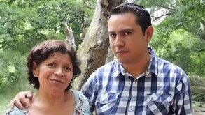 Un hombre serio y una mujer con cara de extrañeza posan para una fotografía abajo de un árbol.
