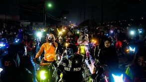 Gran grupo de motociclistas en una rodada nocturna en la calle. Muchos de ellos llevan disfraces y máscaras de Halloween o de terror, con luces delanteras y foc