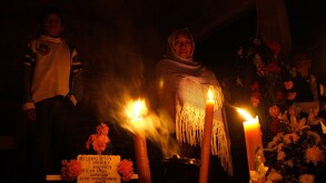 una mujer y un niño en un panteón con veladoras y flores de cempasúchil por día de muertos