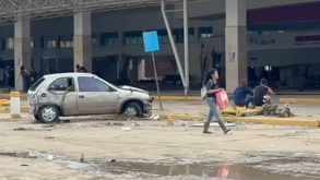 Automóvil destrozado junto a personas sentadas en una central de autobuses devastada por una inundación en Poza Rica, Veracruz.