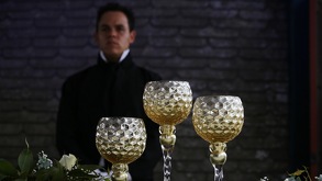 Un hombre vestido de manera elegante parado detrás de unas copas.