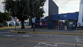 Vista exterior de la entrada principal a la Prepa UNIVA, con el logo azul en un arco. Se ven árboles, un cartel de evento de Halloween, un letrero de 