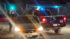 Carro gris con las puertas abiertas y las luces encendidas, camioneta de la policía muncipal de Torreón y una mujer al fondo.