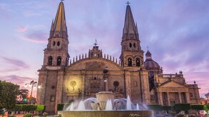 Vista frontal de la Catedral de Guadalajara durante el amanecer con una fuente al frente y árboles alrededor