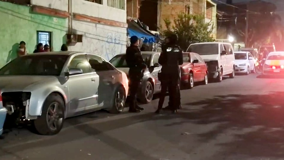 Policías de Guadalajara en el lugar del ataque con casas y automóviles estacionados alrededor y un taxi viniendo de fondo