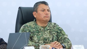 Hombre con las manos cruzadas, vestido con un traje verde militar.