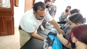 Un hombre con gafas y camisa blanca, posiblemente un instructor o embalsamador, guía a un grupo de estudiantes uniformados en una práctica o clase de tanatoprax