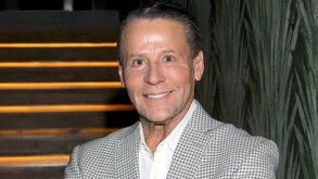 Alfredo Adame sonriendo para la foto, vestido con un saco de cuadros color gris.