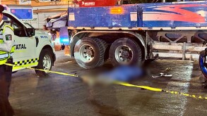 Cuerpo del ciclista que fue arrollado por un camión cubierto por manta azul debajo de las llantas del vehículo y a un lado una patrulla de la Policía Vial