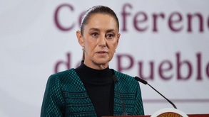 Mujer vestida de playera negra con saco verde, frente a una tarima con un micrófono.