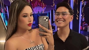 Una mujer tomando una fotografía con su celular; junto a ella, un hombre con lentes sonriendo.