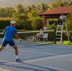 Una pareja de dobles en tenis disputa un partido con juez incluido al atardecer.