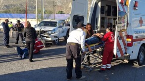 Ambulancia de la Cruz Roja, paramédicos atendiendo a una pareja lesionada, un hombre está sobre el pavimento y una mujer está en una camilla.
