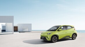 Un coche eléctrico BYD Seagull de color verde lima o amarillo brillante está estacionado en una plataforma de concreto junto a una estructura blanca minimalista