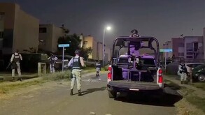 Patrulla estacionada y elementos de la Policía de Tlajomulco y Fiscalía de Jalisco resguardando una zona de noche dentro del fraccionamiento con casa alrededor