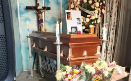 Cajón fúnebre con veladras en las cuatro esquinas y arreglos florales