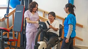 dos mujeres jóvenes dan fisioterapia a una mujer mayor que padrece artritis