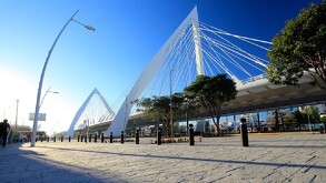 Vista del Puente Atirantado Matute Remus en Guadalajara al atardecer o amanecer. La estructura blanca con cables domina la escena, con un andador de piedra y un