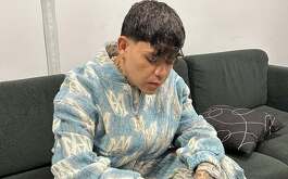 Junior H con la mirada hacia abajo sentado en un sillón