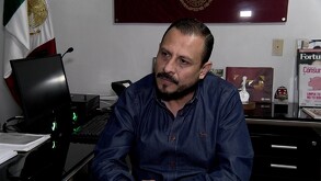 El titular de la Profeco en una entrevista. Es un hombre con barba de candado y camisa de mezclilla, sentado en un escritorio de oficina con la bandera de Méxic