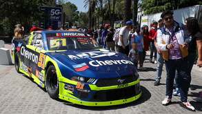un joven se toma una fotografía frenta a un auto de la nascar en exhibición en puebla