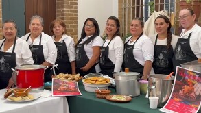 Mujeres con mandiles negros muestran ollas con tamales y atole.