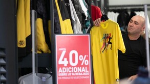 Hombre calvo sostiene una playera amarilla en oferta en una tienda de ropa.