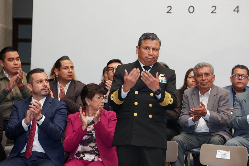 Hombre vestido con traje de vicealmirante saluda a una multitud a sus espaldas.