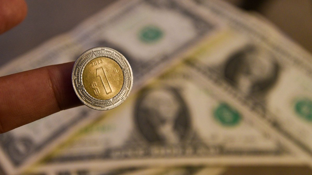 Moneda de 1 peso mexicana y billetes de dólar