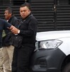 Hombre vestido de negro recargado sobre un auto blanco con las siglas de la Fiscalía de Puebla.