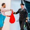 Pilotos de avión saludan y reciben bolsas de regalo rojas y azules de un promotor en la pasarela de un aeropuerto. Esto probablemente marca la inauguración de n