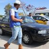 Hombre con sombrero camina frente a dos taxis estacionados afuera del Estadio Cuauhtémoc de Puebla.