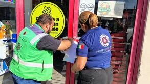 Un hombre con chaleco verde y una mujer con playera azul pegando sellos de clausura en una puerta