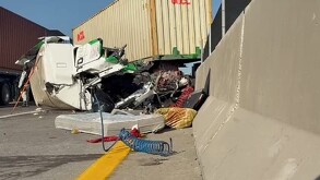 Accidente de carretera: un tráiler blanco volcó, con su cabina destrozada y la caja del contenedor horizontal. Un oficial y personal de rescate inspeccionan la