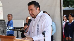Hombre con camisa blanca con un micrófono en la mano, hablando desde una tarima.