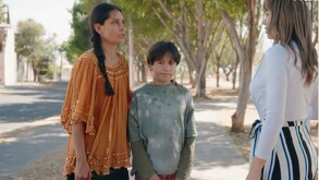 Dos madres de familia aparecen junto a un niño, la primera de ellas aparece con un sueter cafe y el niño con una playera verde, ambas estan platicando.