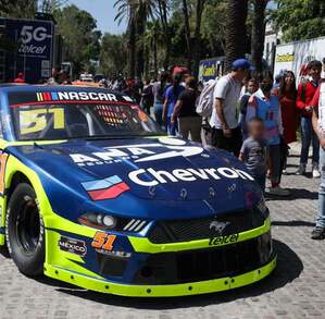 un joven se toma una fotografía frenta a un auto de la nascar en exhibición en puebla