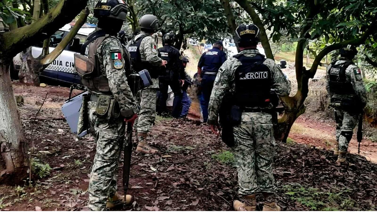 Una incautación de armas y equipo militar. En una lona se muestran dos fusiles AK-47, múltiples cargadores, y municiones sueltas junto con chalecos camuflados y