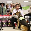 Dos agentes de seguridad con perros de detección se agachan frente a bolsas de alimento para mascotas. Detrás de ellos, un grupo de funcionarios y ciudadanos so