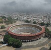 Vista aérea de la Plaza de Toros El Nuevo Progreso de Guadalajara, rodeada de áreas de estacionamiento y casas. El cielo está nublado y una ligera lluvia cae so