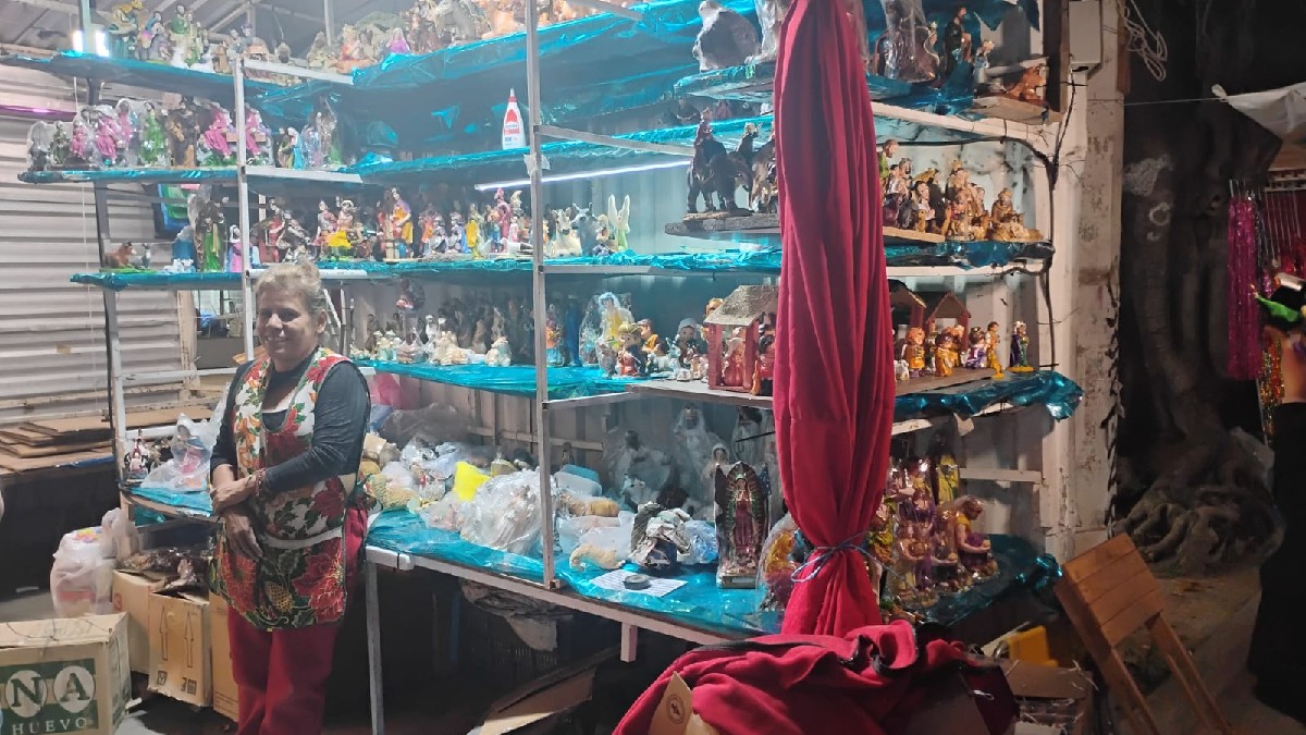 Tianguis o mercado nocturno con un pasillo cubierto por una lona blanca. Puestos llenos de adornos navideños, luces de colores y guirnaldas están a la venta con