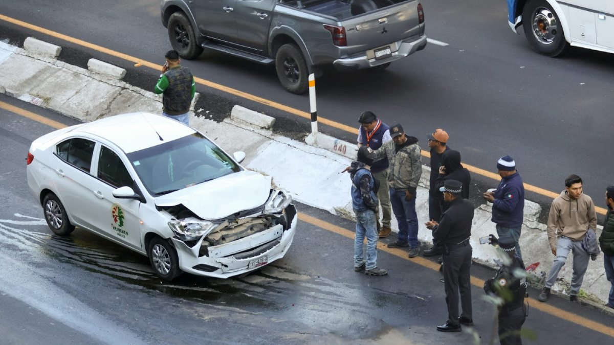Un vehículo blanco accidentado, y al lado un conjunto de personas que observan el accidente.