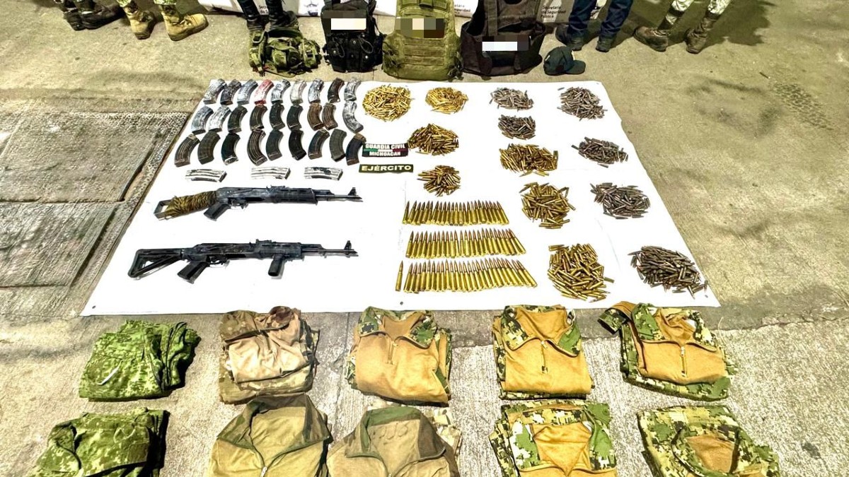 Una incautación de armas y equipo militar. En una lona se muestran dos fusiles AK-47, múltiples cargadores, y municiones sueltas junto con chalecos camuflados y