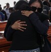 Mujeres vestidas de negro abrazándose frente a un féretro, durante un funeral.