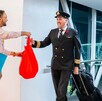 Pilotos de avión saludan y reciben bolsas de regalo rojas y azules de un promotor en la pasarela de un aeropuerto. Esto probablemente marca la inauguración de n