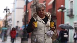 una mujer abrigada camina por el centro de puebla con dos cafés en las manos
