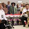 Dos agentes de seguridad con perros de detección se agachan frente a bolsas de alimento para mascotas. Detrás de ellos, un grupo de funcionarios y ciudadanos so